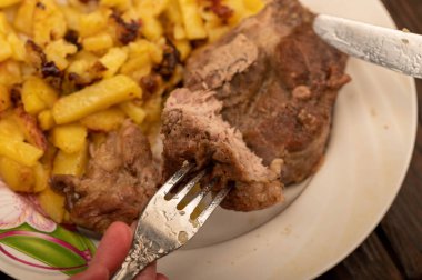 Birisi çatal ve bıçakla bir tabak kızarmış patatesle sulu bir parça et kesiyor. Seçici Odaklamayı Kapat