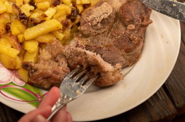 Birisi çatal ve bıçakla bir tabak kızarmış patatesle sulu bir parça et kesiyor. Seçici Odaklamayı Kapat