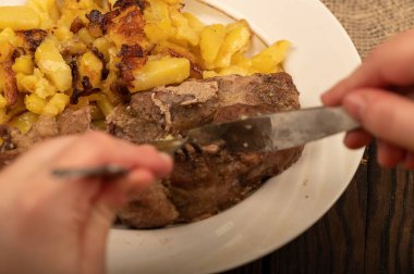 Birisi çatal ve bıçakla bir tabak kızarmış patatesle sulu bir parça et kesiyor. Seçici Odaklamayı Kapat