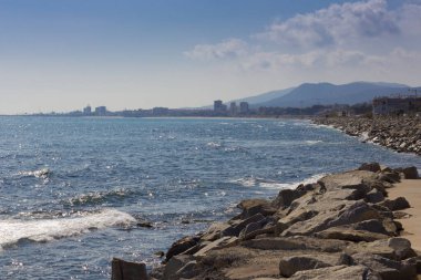 Akdeniz 'de kayalık bir dalgakıran, mavi gökyüzü ve su ve dalgaların üzerinde yeşil deniz yosunları, denizin dalgaları tarafından yenildi..