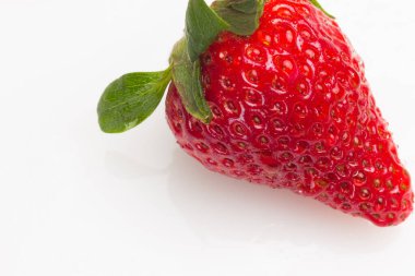 Beyaz arka planda mevsimlik çileklerin yakın çekimleri. Yeşil yaprakları ve su damlaları olan çilekler. Çilek tohumlarının Macro fotoğrafı. Sağlıklı ve tatlı meyve