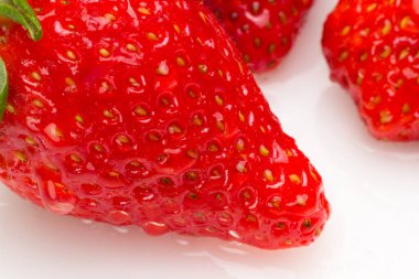 Beyaz arka planda mevsimlik çileklerin yakın çekimleri. Yeşil yaprakları ve su damlaları olan çilekler. Çilek tohumlarının Macro fotoğrafı. Sağlıklı ve tatlı meyve