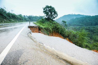Şiddetli yağmurların yol açtığı heyelan, bozuk yol asfaltına neden olur. Sokakta yıkılmış çimento. Toprak kaymasından çıkan çatlak yol sağanak yağış yüzünden mahvoldu.