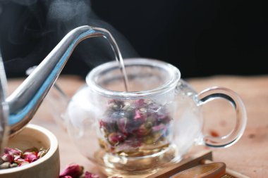 Şeffaf camlı gül çayı ve tahta üzerinde kurumuş gül çiçeği olan sürahi. Aroma, çiçek çayı ile sağlığa iyi gelir..