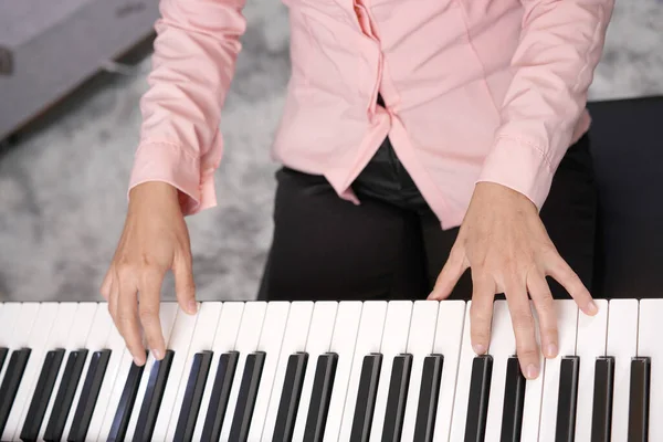 Adult woman plays electronic piano with note sheet. Newby pianist practicing and learning how to play song.
