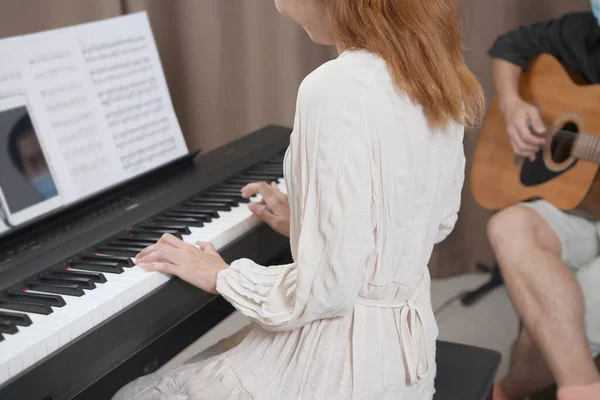 Adult women plays electronic piano with note sheet. Newby pianist practicing and learning how to play song.