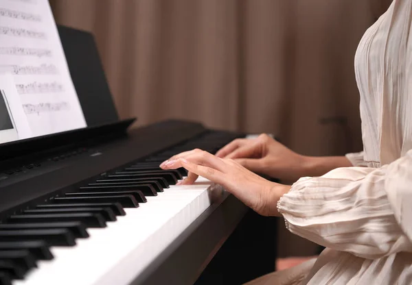 Adult women plays electronic piano with note sheet. Newby pianist practicing and learning how to play song.