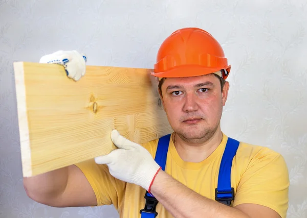 Male construction worker in a hard hat with a wooden board