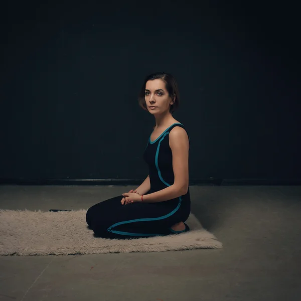 Mulher praticando ioga contra uma parede texturizada escura — Fotografia de Stock