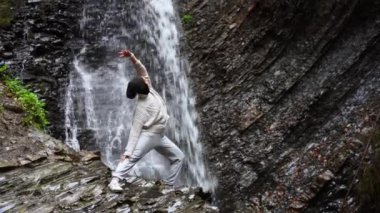 Yoga yapan bir kadın dağ gölünde arka planda şelale yapıyor. Açık hava meditasyonu.