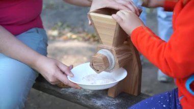 Kadın çocuklara el yapımı ahşap değirmeni kullanmayı öğretiyor. Tanımlanamayan kişi