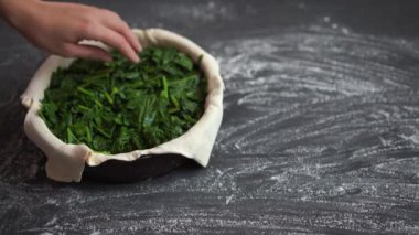 Kadın turtayı taze ıspanakla doldurur ve içini hamurla doldurur..