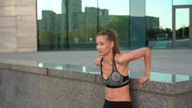 Kadın ısınıyor, trisepsleri kaldırıyor şehir arka planında egzersiz yapıyor. 