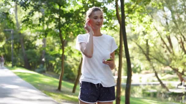 Vrouw zet oortjes op om muziek te luisteren voor het joggen zomer park — Stockvideo