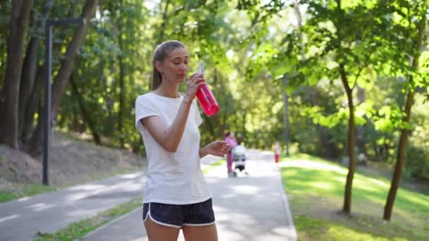 Femeia bea apă sticlă roșie după antrenament de dimineață . — Videoclip de stoc