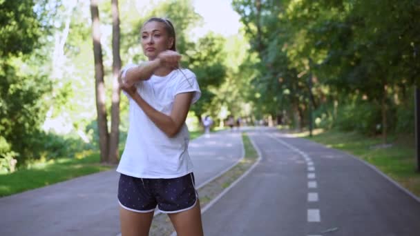 Женщина, бегущая с протянутыми руками перед утренней тренировкой в летнем парке — стоковое видео