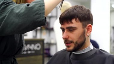 Berber dükkanında oturan yakışıklı mavi gözlü adam. Kuaför kadın onun saçını kesiyor. Kadın berber.. 