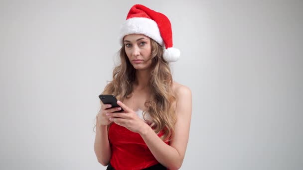 圣诞女性圣诞帽白色工作室背景，手持智能手机 — 图库视频影像