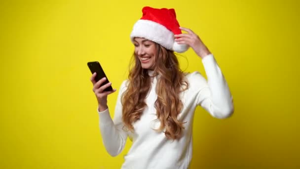 Nő Karácsony Santa Hat fehér pulóver sárga stúdió háttér okostelefon a kezében