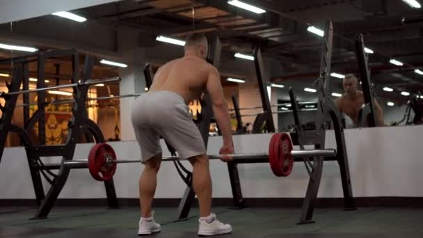 Svalnatý atletický kulturista fitness model stojící před zrcadlem zpět na kameru trénink činka činka vnitřní tělocvična — Stock video