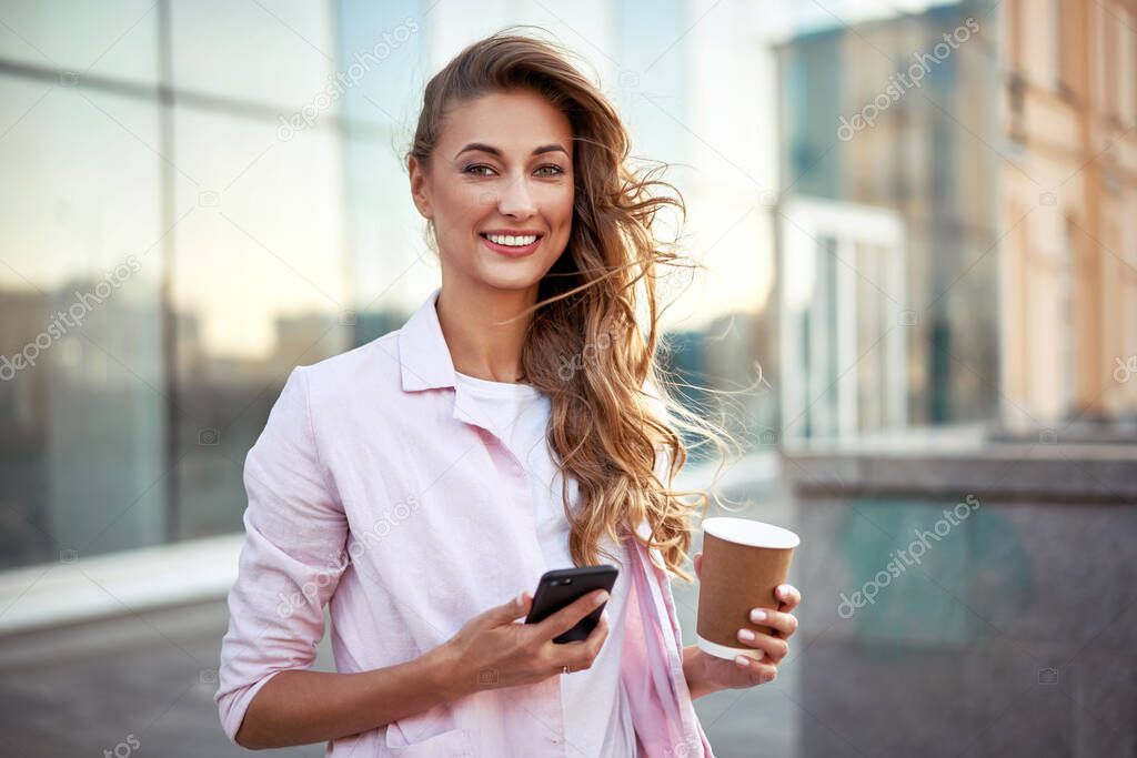 Businesswoman standing summer day near corporate building using smartphone teeth smiling Business person Outdoors Successful european caucasian woman freelancer dressed white shirt pink jacket