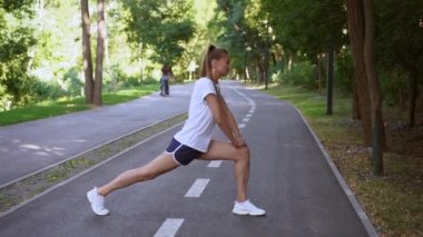 Kadın koşucu yaz parkında egzersiz yapmadan önce bacaklarını esnetiyor.