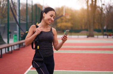 Trx spor sahası kullanan kız sporcu eğitimi. Karışık ırk genç yetişkin kadın spor süspansiyon sistemi. Açık havada esnemek için sağlıklı bir yaşam tarzı. Vücut makineni yap                            