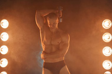 Dambıl sallayan genç bir atlet, triseps çalışması, dumanlı bir arka plan, sağlıklı yaşam tarzı konsepti. Spor ve zindelik lambası