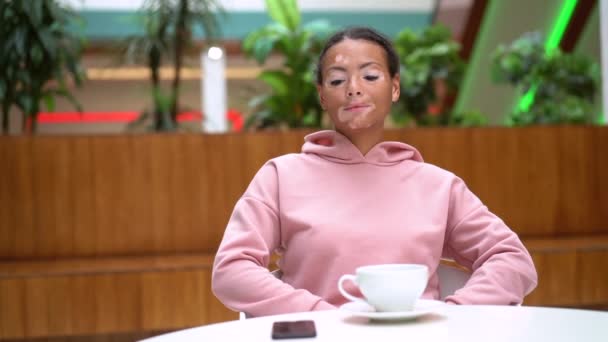 Negro mujer afroamericana con problemas de pigmentación de la piel vitiligo interior vestido rosa sudadera con capucha beber té en la mesa — Vídeo de stock