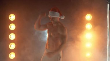 Zafer jesti. Noel Baba şapkalı heyecanlı kaslı adam, kazanan hareketi gösteriyor, arka planda lambalar yanıyor.