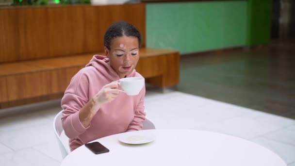 Svart afrikansk amerikansk kvinna med vitiligo pigmentering hudproblem inomhus klädd rosa hoodie — Stockvideo