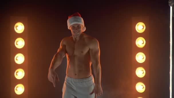 Świąteczne tańce. Wesoły muskularny facet w kapeluszu Santa zabawny taniec nad oświetlonymi lampami — Wideo stockowe