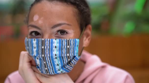 Schwarze Afroamerikanerin mit Vitiligo-Pigmentierung Hautproblem drinnen gekleidet rosa Kapuzenpullover und schützende Gesichtsmaske — Stockvideo