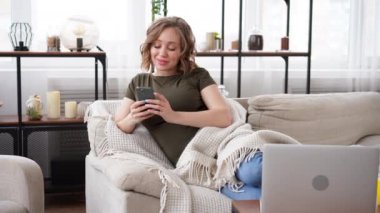 Kanepede uzanmış elinde akıllı telefonu tutan hamile bir kadın. 