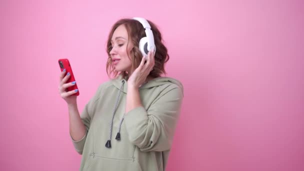 Щасливі зуби посмішка жінка слухати музичні навушники на рожевому фоні — стокове відео