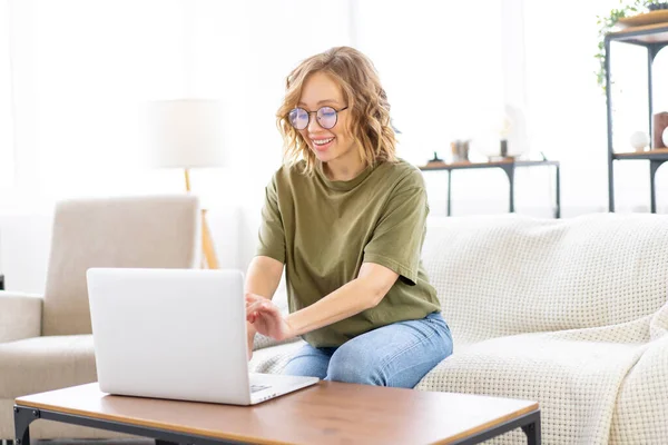 Gözlüklü Bir Kadın Dizüstü Bilgisayar Kullanıyor Klavye Kullanıyor Kanepeye Oturuyor — Stok fotoğraf