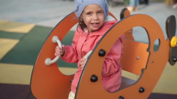 Дитя. Девочка играет на детской площадке. Качели на игрушечном деревянном автомобиле и весело провести время — стоковое видео