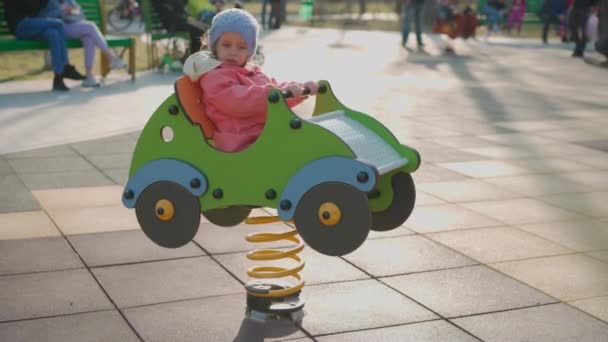 Дитя. Девочка играет на детской площадке. Качели на игрушечном деревянном автомобиле и весело провести время — стоковое видео