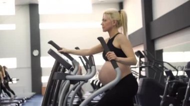 Hamile kadın, eliptik antrenörü spor salonunda çalışan simülatörde çalıştırıyor. 