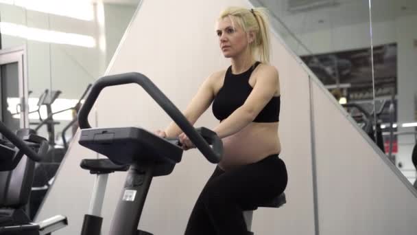 Bicicleta de ejercicio de entrenamiento de mujer embarazada en gimnasio Ejercicios de cardio en simulador de carrera — Vídeo de stock