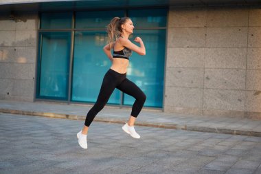 Şehir geçmişine karşı atlayan ve kaçan bir kadın. Spor giyim sektöründe kadın model açık havada egzersiz yapıyor. Spor motivasyonu