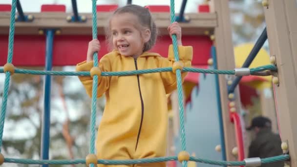 Criança. A menina brinca no parque infantil. Subir quadro de escalada — Vídeo de Stock