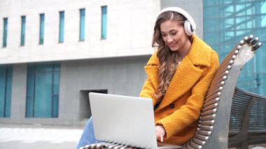 İş kadını gözlük takar müzik kulaklığı takar dışarıda oturur, dışarıda dizüstü bilgisayar kullanır.