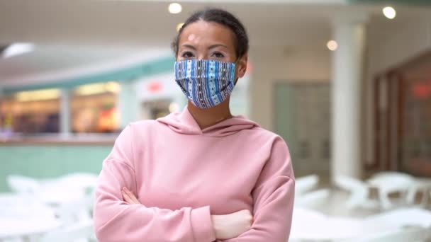 Mujer afroamericana negra con problema de pigmentación de la piel vitiligo con capucha rosa vestida en interiores y mascarilla protectora — Vídeos de Stock