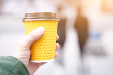 Tanımlanamayan bir adam elinde sarı kağıt bardakla elinde kahveyle Blured Caddesi arka planında
