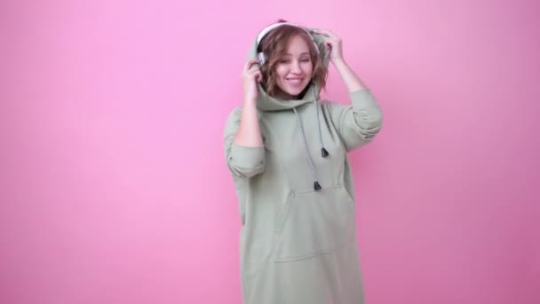 Szczęśliwy zęby uśmiech kobieta słuchać muzyki słuchawki na różowym tle ubrany oversize bluza — Wideo stockowe