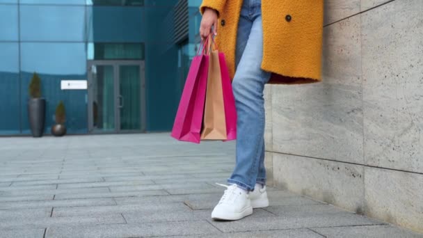 Zakelijke vrouw met boodschappentassen gekleed gele jas wandelen buiten corporatieve gebouw achtergrond — Stockvideo