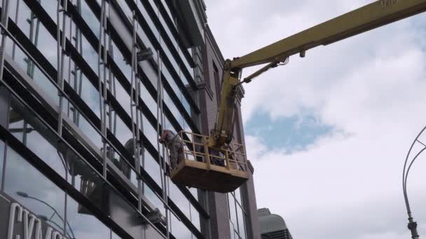 Ucrania, Kharkov, mayo 2021 Hombres en el trabajo reparación de la fachada del edificio a la altura en la cuna de elevación. — Vídeo de stock