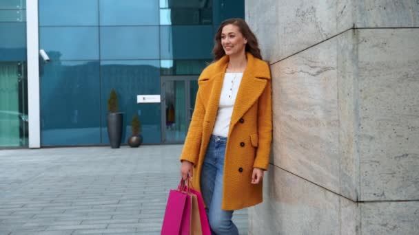 Donna d'affari con shopping bags vestito giallo cappotto camminare all'aperto corporativo edificio sfondo — Video Stock