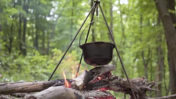 Sombrero Bowler con deliciosas gachas se para en el trípode durante la fogata mientras camina por los bosques — Vídeo de stock